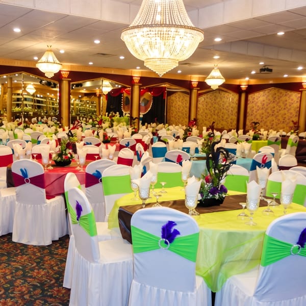 A large, ornate banquet hall with many tables set with colorful linens and white chair covers.