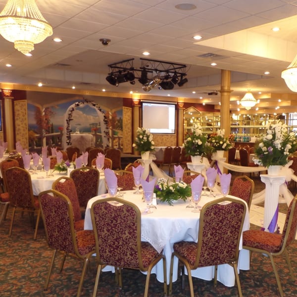 A large banquet hall with round tables set with white tablecloths, purple napkins, and floral centerpieces.