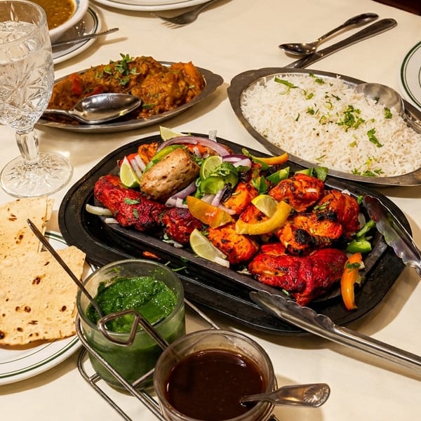 A table set with Indian dishes, including tandoori chicken, rice, curry, naan, and sauces.