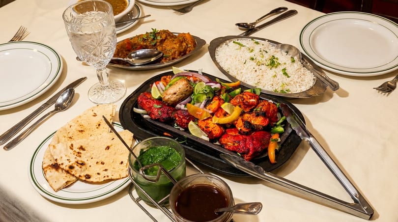 A table set with Indian dishes, including tandoori chicken, rice, naan, and curries.