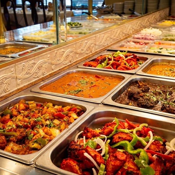 A buffet line with various Indian dishes in metal serving trays, including curries and tandoori chicken.