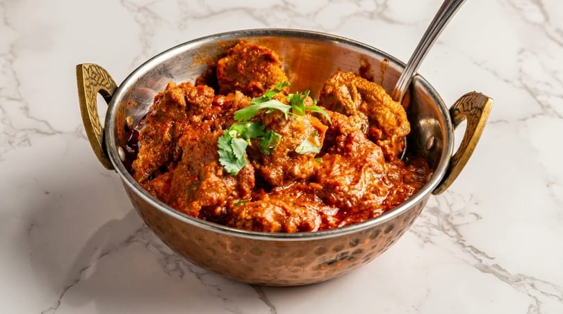 A copper bowl filled with rich, red Indian curry and garnished with fresh cilantro.